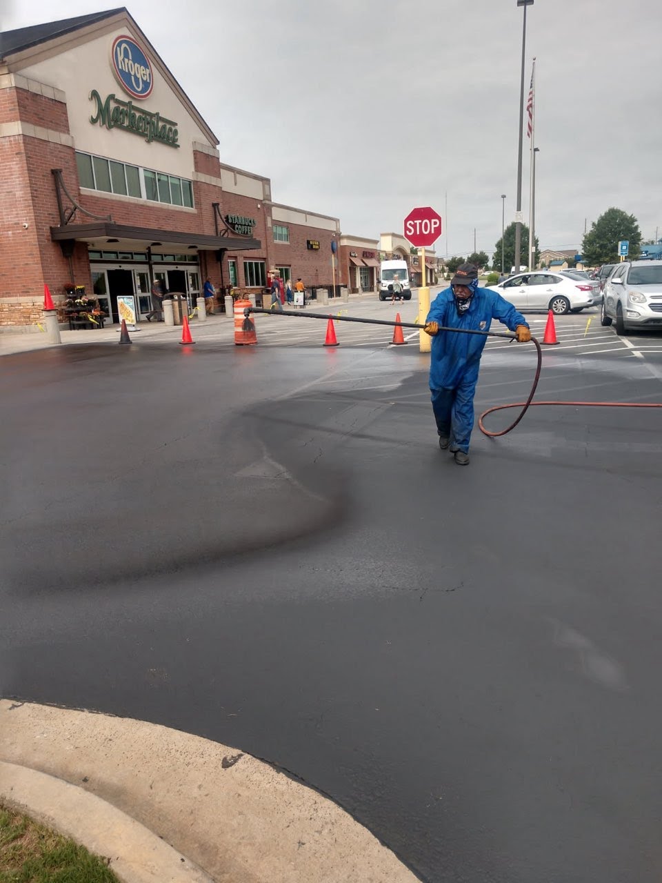 Fresh paved commercial asphalt parking lot, work crew setting out orange cones